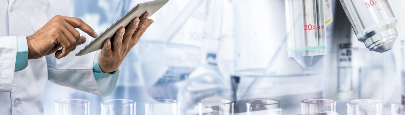 Science research and technology concept - Scientist holding tablet computer with scientific instrument microscope and chemical test tube in lab background.